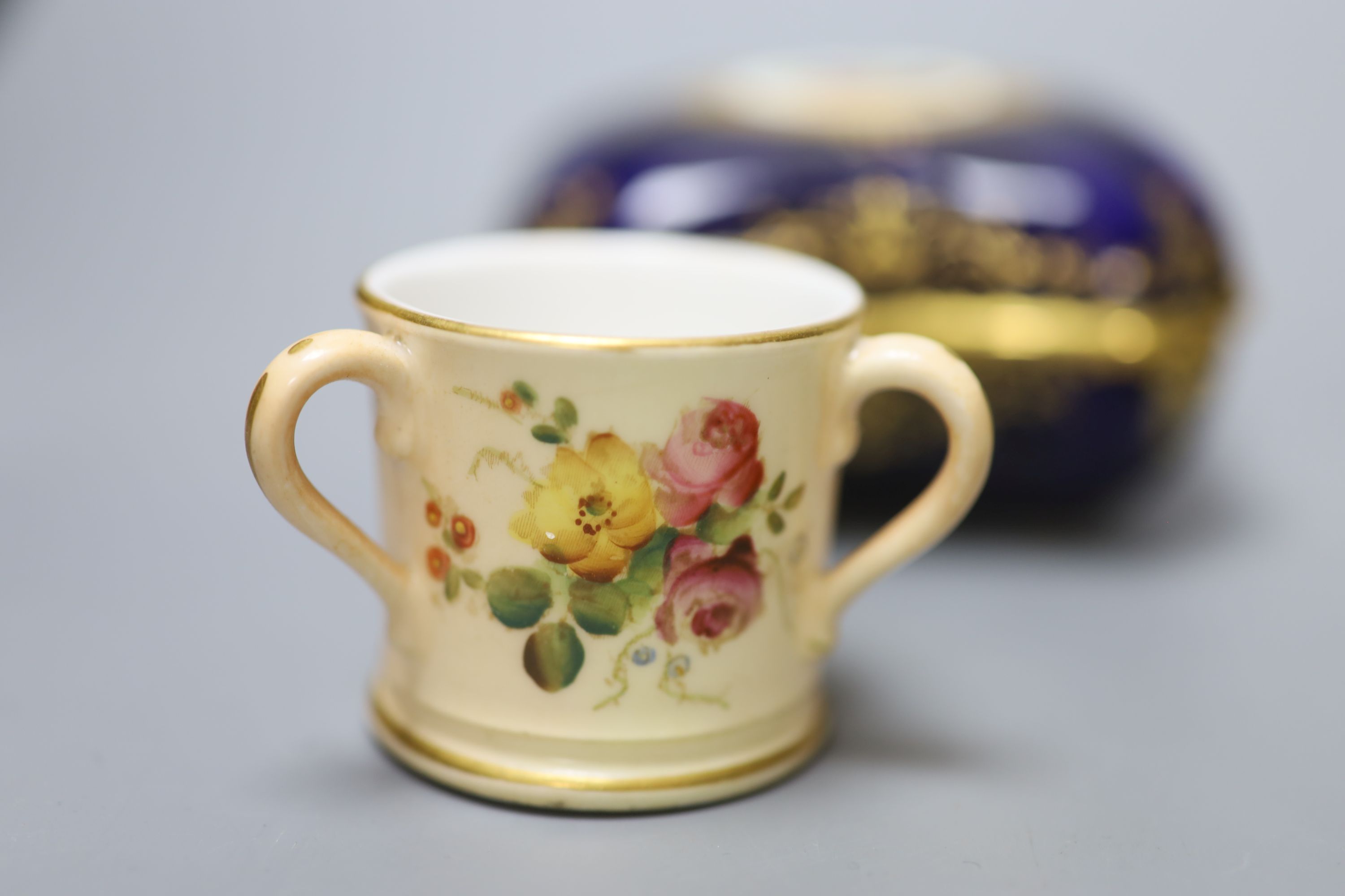 An early 20th century Coalport box and cover painted with a bird on a blue ground, a Coalport miniature gilt ground mug with landscape,